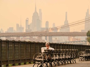 A person on a bench reads a newspaper as wildfire smoke from Canada causes hazy conditions on July 16, 2026 in New York.