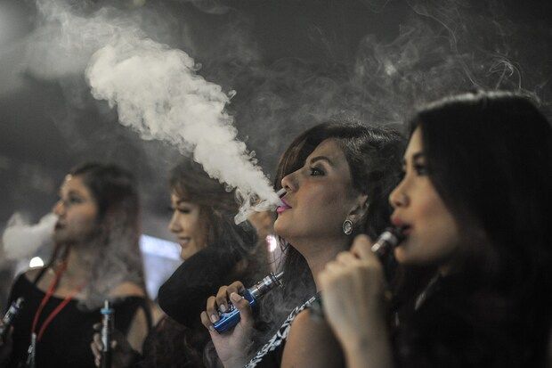 Promoters smoke electronic cigarettes during the VapeFair in Kuala Lumpur.