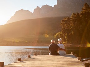 Romantic Senior Couple Sitting On Wooden Jetty By Lake