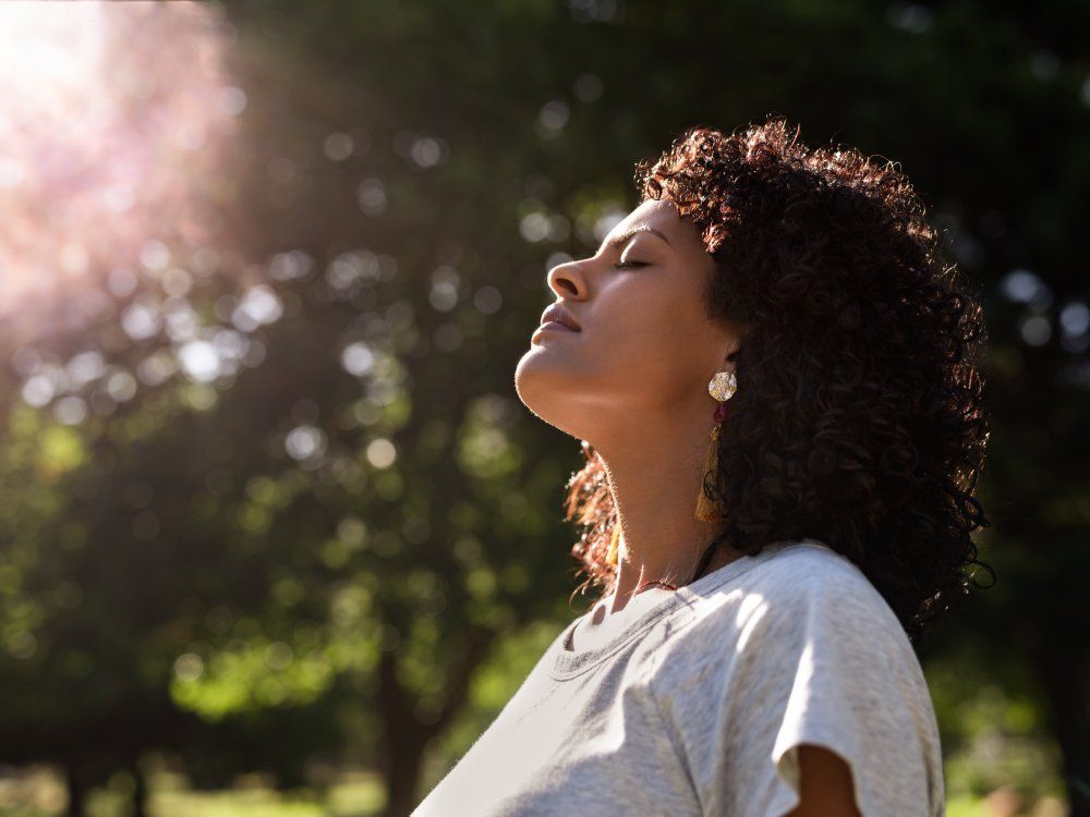 Young woman standing outdoors feeling the sun on her face