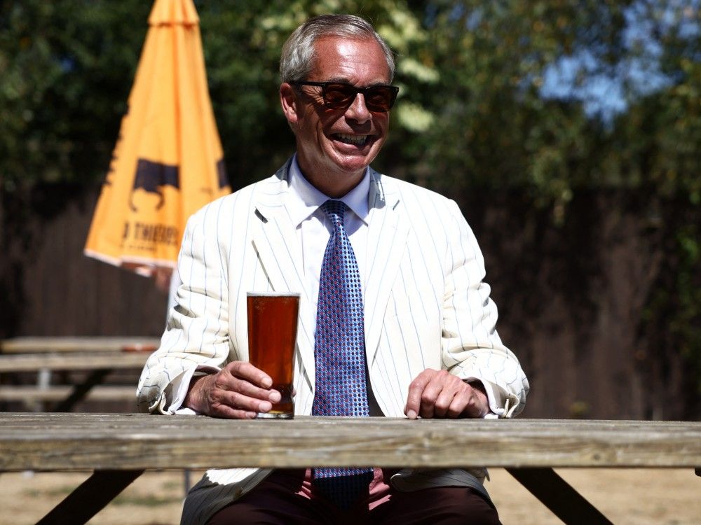 Reform UK leader Nigel Farage sits and poses with a pint of beer in the garden of The Ship pub after casting his vote in the Clacton by-election earlier in the morning, in the village of Kirby-le-Soken, Essex, England, Thursday, Aug. 13, 2026.