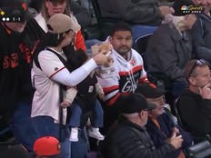 A mother returns to her seat while holding a baby and food during a San Francisco Giants game.