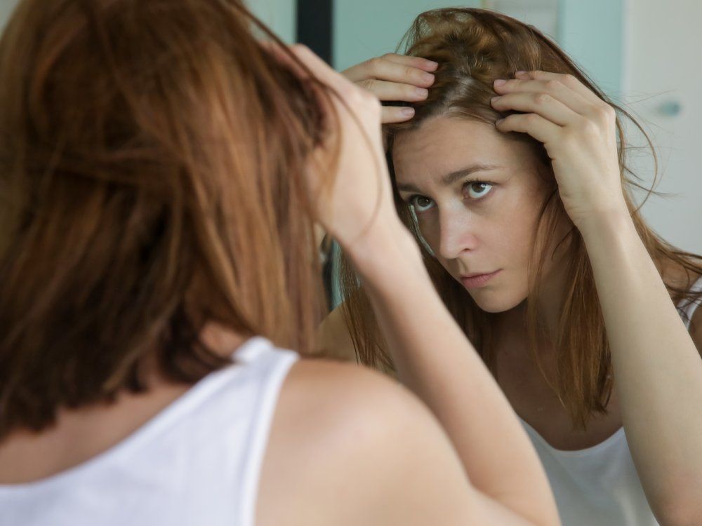 Portrait of a beautiful young woman examining her scalp and hair in front of the mirror, hair roots, color, grey hair, hair loss or dry scalp problem