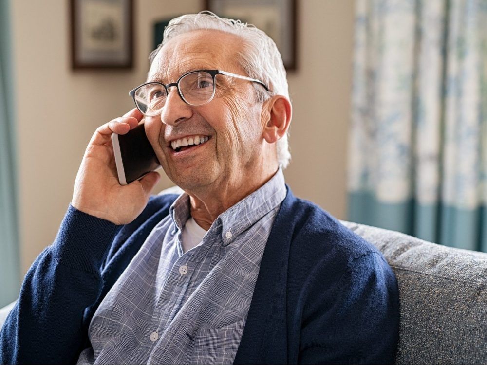 A smiling older man talks on a phone.