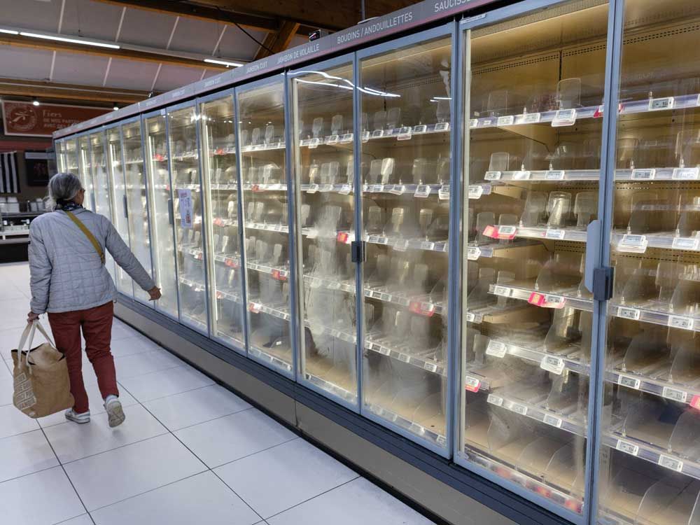 A woman walks past empty fresh-food refrigerators at an Intermarche supermarket in Nevez, western France, on Oct. 12, 2026, following a cyberattack affecting the French supermarket chains Intermarche and Cooperative U that caused their refrigerators to defrost.