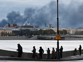 Fishermen fish on the Neva River as smoke rises above the city following an air attack on the oil terminal in St. Petersburg on Oct. 18, 2026, amid the ongoing Russian-Ukrainian conflict.