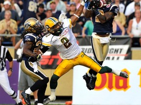 Fred Stamps, centre, is tugged on by Jonathan Hefney as Jovon Johnson grabs an interception on Friday night in Winnipeg.