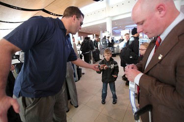 Winnipeg Blue Bombers DT Doug Brown hands a signed souvenir football to seven-year-old fan Justis Hellegards as players prepared to leave Winnipeg Richardson International Airport to play in the CFL Grey Cup in Vancouver. At right is Bombers head coach Paul LaPolice. (JASON HALSTEAD, Winnipeg Sun)