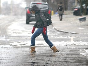 A pedestrian copes with large puddles filled with slush in Kingston, Ont. (Michael Lea/QMI Agency Files)
