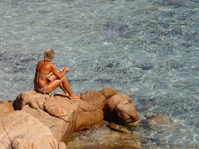A woman sits by the rocks at the Ramizzo beach in the so called "Emerald Coast" of the Sardinia island in Italy July 7, 2011. REUTERS/Max Rossi