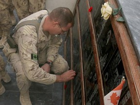 A soldier places a poppy on a plaque during  at the cenotaph Remembrance Day ceremonies at Kandahar Air Field.