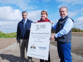 Tom Looby, left, vice--president of Hayhoe Homes, holds the sign Wednesday for the new Orchard Park South Trail with Mayor Heather Jackson and Walter Hayhoe, president of Hayhoe Homes. Hayhoe officially turned over to the city a five-acre parcel of land off Southdale Line for the trail.