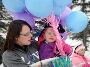 Three-year-old Madison Balcom-Ross is held by her mother, Trina Ross, during SMS awareness day Saturday at Muskoseepi Park. Family and friends gathered to release balloons to raise awareness for the rare chromosome disorder that affects one in every 25,000 children. (Adam Jackson/Daily Herald-Tribune)