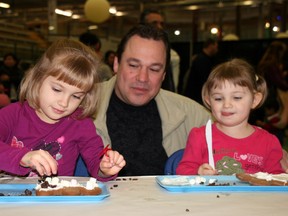 Elizabeth, 4, and Emily, 2, take time out of a busy Sunday to decorate gingerbread men at the Festival of Trees with their dad, Mark McConachie. AMANDA RICHARDSON/TODAY STAFF