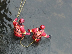 Two firefighters from the marine rescue unit wade into the Thames River near Adelaide and Ada streets to retrieve a suspected firearm Saturday. (DALE CARRUTHERS, The London Free Press)