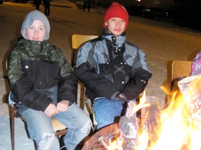 Luc Lessard, left, and his friend Pler Say Moo, both 11, warm themselves at the bonfire lit and maintained by Sangudo firefighters at the Sangudo Christmas Blitz on the evening of Friday, Nov. 30. The annual event featured rides, games for children, vendors and food.