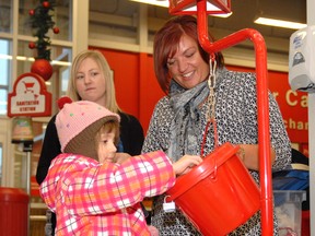 Lauren Kirkham, 5, donates some change in a Salvation Army kettle at Canadian Tire on Tuesday afternoon as her grandpa Harold Anderson (out of photo) and volunteers Jessie Urness and Holly Sorgen look on. (Patrick Callan/Daily Herald-Tribune)