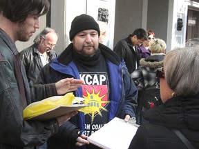 Mike Oullette, centre, a member of the Kingston Coalition Against Poverty, holds a letter he was asking people to sign on Princess Street Thursday, calling for the provincial government to reverse its intention to cut a social assistance program. (Michael Lea The Whig-Standard)
