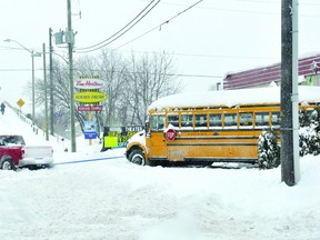 A four-wheel drive pickup gives a stuck school bus a tug to help it make it through the Casual Living parking lot onto William Street Thursday morning. (DARCY CHEEK/The Recorder and Times)