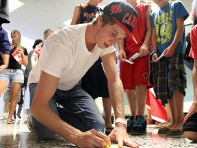 Olympic bronze medallist Derek Drouin kneels on the floor of Sarnia Chris Hadfield Airport to sign autographs for a group of kids after returning from the 2012 Summer Olympics in London on Monday. Drouin, from Corunna, won bronze in the high jump, Canada's first medal in the event since 1976. PAUL OWEN/ THE OBSERVER/ QMI AGENCY