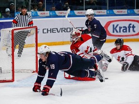Jake McCabe of the U.S. goes flying past Canada’s goalie Jordan Binnington and player Phillip Danault, right, at a semifinal game at the World Junior Hockey Championships in Ufa, Russia, on Thursday.