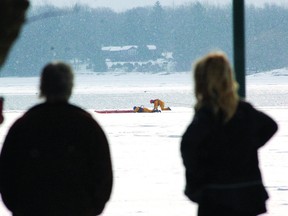 Bystanders watch from the shore as Brockville firefighters attempt to reach a man who slipped beneath the ice shelf on the St. Lawrence River on Wednesday morning. (DARCY CHEEK/The Recorder and Times)