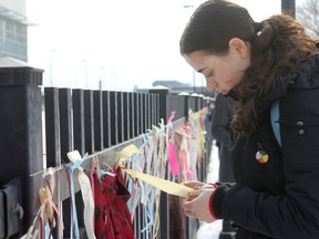 Renata Colwell, a Queen's University student, secures a pin on a ribbon hung in front of the Kingston Police station Thursday. Ribbons and skirts were hung from a fence to represent the more than 600 missing and murdered indigenous women in Canada.
Danielle VandenBrink/The Whig-Standard