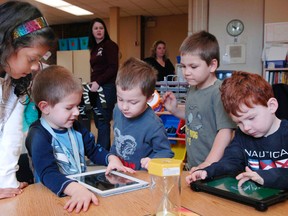 Gabriella Ferrao, 6, watches as Major Ballachey School kindergarten students Austin Detheridge, Jeremy Meitz, Chase Racette and Logan Smith work on iPads in Brantford on Friday. Ferrao donated $500 to support a fundraiser that would see several classroom sets of the tablets purchased to support learning at the school. (HUGO RODRIGUES The Expositor)