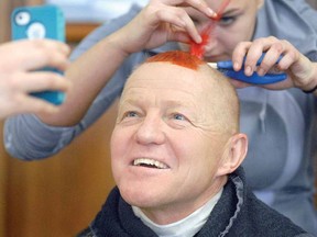 Stratford Northwestern principal Martin Ritsma checks out a photo of himself as cosmetology student Kaitlyn Cullum attaches a feather to his hair at a Mohawks for Meningitis event at the school Thursday. (SCOTT WISHART The Beacon Herald)