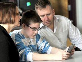 Helen Allin, left, and Carson Warrener, get a lesson in iPad technology from Colin Price, 13, a Grade 8 student at Queen Elizabeth Public School where the Warrener family has donated 40 iPad mini's. The iPad docking station was dedicated to the memory of Allin's husband Dave, a long time coach at the school who died in January. (DIANA MARTIN, The Daily News)