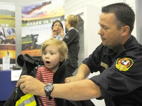 County of Grande Prairie fire chief Everett Cooke dons Markus Schroeder, 3, with fire gear during the county's open house event at Crystal Creek Hall last year. The events were such a hit last year that the County is reviving them again. (DHT file photo)