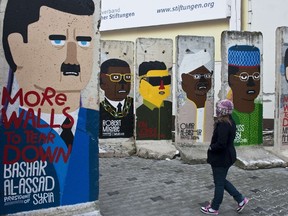 A girl looks at concrete slabs from the former Berlin Wall painted with likenesses of the world's most notorious dictators, by French artist Guillaume Kashima, near the city's Checkpoint Charlie area in Berlin. JOHN MACDOUGALL/AFP Photo
