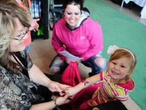 Kinley Clease, 2, receives a glitter tattoo by Sparkle Tattoo Inc. artist Jo-Anne Kitching while Jennifer Peterson looks on at the Women's Show at the Grande Prairie Crystal Centre, Sunday, March 25, 2012. (DHT file photo)