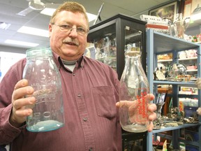 Ken Brown holds some old glass milk containers in his Main Street shop Friday morning. Brown is hoping his business, Brown's Vacuums, Antiques & Collectibles on Main Street, is one of several places featured in the hit reality show Canadian Pickers.