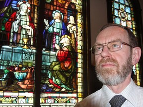 John Young, an assistant professor and chairman of the theology program at Queen's University, stands in the Theological Hall chapel in front of a stained glass image of Jesus breaking bread with travelers after meeting them on the road to Emmaus following his resurrection.
Michael Lea The Whig-Standard