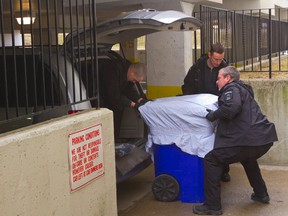 Forensics officers and coroner's staff prepare to lift a large plastic canister carrying human remains into the coroner's van at the parking entrance at 85 Fiddlers Green Rd. in London. (MIKE HENSEN/QMI AGENCY)