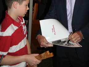 Hockey legend Paul Henderson, right, autographs a book about the 1972 Summit Series for 10-year-old Andrew Skinner. Henderson, and his wife Eleanor, shared the podium as the keynote speakers for the 33rd-annual Athletes in Action held at the Porcupine Dante Club Wednesday night.