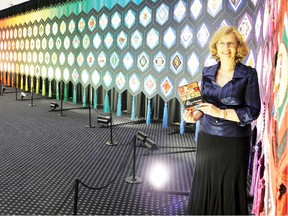 Esther Bryan, founder of the Quilt of Belonging, stands by the large quilt while holding a copy of the new documentary about the tapestry during the film’s official launch at the Nav Centre on Thursday. The quilt and documentary will be on display over the weekend from 10 a.m. to 5 p.m. at the Nav Centre.  
Staff photo/ERIKA GLASBERG