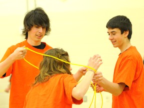 Grade 9 student Cain Nicolet, left, and Tyler Shkwarok, Grade 8, right, help Grade 7 Courtney Romancewicz out of a knot in complete silence during a ‘We are silent’ campaign day at École St. Gerard Thursday. (Adam Jackson/Daily Herald-Tribune)