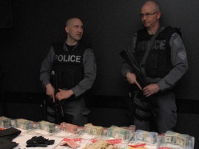 Const. Kevin Tower and Staff-Sgt. Kerry McCowell stand Friday, April 26, 2013, beside a large haul of weapons, body armour and cash police seized when they arrested three suspects wanted in connection with a string of "takeover-style" bank robberies. (SHAWN JEFFORDS/Toronto Sun)