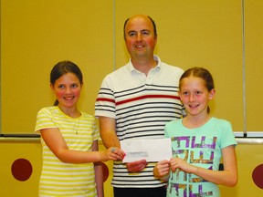 Holy Cross School Grade 6 students Cailyn Poole (left) and MacKenzie Gill (right) present  Habitat for Humanity Director of Family Services Armand Mercier with a cheque for $1,263, raised in a Lenten social justice endeavour.