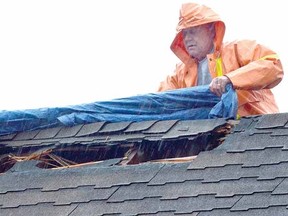 Murray Feltz drapes a tarp in pouring rain after a lightning strike blasted a gaping hole in the roof of the Valu-mart garden centre in downtown Mitchell Tuesday afternoon. (SCOTT WISHART, The Beacon Herald)