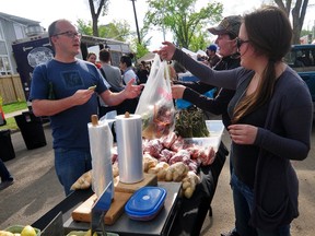 Ed Elyn, left, buys a bag of asparagus from Patsy Tomkins, far right, and Jentre Brault from the Steve & Dan's Fresh B.C Fruit table as shoppers gathered along 108 Avenue and 124 Street  for the opening day of the 124 Grand Market on Thursday, May 23, 2013. TREVOR ROBB Edmonton Examiner