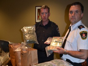 Const. Jeremy Mighton, left, of the criminal investigations unit of the Saugeen Shores Police and Insp. Vince Wurfel of the Owen Sound police show some of the drugs, cash and other items seized in busts in Owen Sound and Port Elgin on Wednesday. (Rob Gowan The Sun Times)