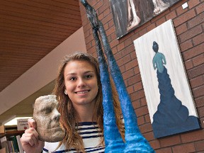 Sixteen-year-old Carah Hager shows her mask "Phantom" and sculpture "The Blue Man," which are featured in North Park Collegiate's  senior art show.  Behind her are paintings "Strength" (top) by MItch Joiner and "The Girl Who Mattered" by Dorian Staats. (BRIAN THOMPSON, The Expositor)