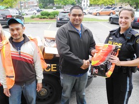 SARAH DOKTOR Simcoe Reformer
Joanna Elliott, secretary of the Windham Community Policing Committee puts a vest onto seasonal worker Carlos Chan as Ernesto Hernandez receives his from Norfolk Const. Shauna Gravefell outside of Food Basics in Simcoe on Friday as part of the committee's safety vest initiative.