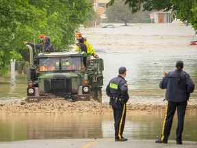 Officials talk as a truck in army camouflage navigates the flooded streets in High River, Alta. on Thursday, June 20, 2013. The Highwood River running through High River was flooding extremely, prompting a town wide evacuation. Lyle Aspinall/Calgary Sun/QMI Agency
