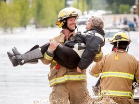 A rescued woman is carried by a firefighter out of a flood zone in High River, Alta. on Thursday, June 20, 2013. The Highwood River running through High River was flooding extremely, prompting a town wide evacuation. Keep following the High River Times for a story about this smile and the firefighter who has become an internet sensation. Lyle Aspinall/Calgary Sun/QMI Agency