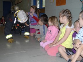 Kirkland Lake Friendly Firefighter Danny Sasseville crawls past Central Public School Kindergarten students so they can hear his equipment and touch it.