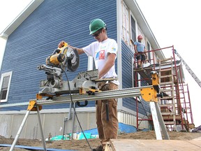 Tom Minnie, centre, a student in the Building Construction Internship Program, cuts a length of siding for the group's latest home, being built on Wolfe Island, as fellow student Harry Stone, left, and teacher Dan Fisher look on.
Michael Lea The Whig-Standard